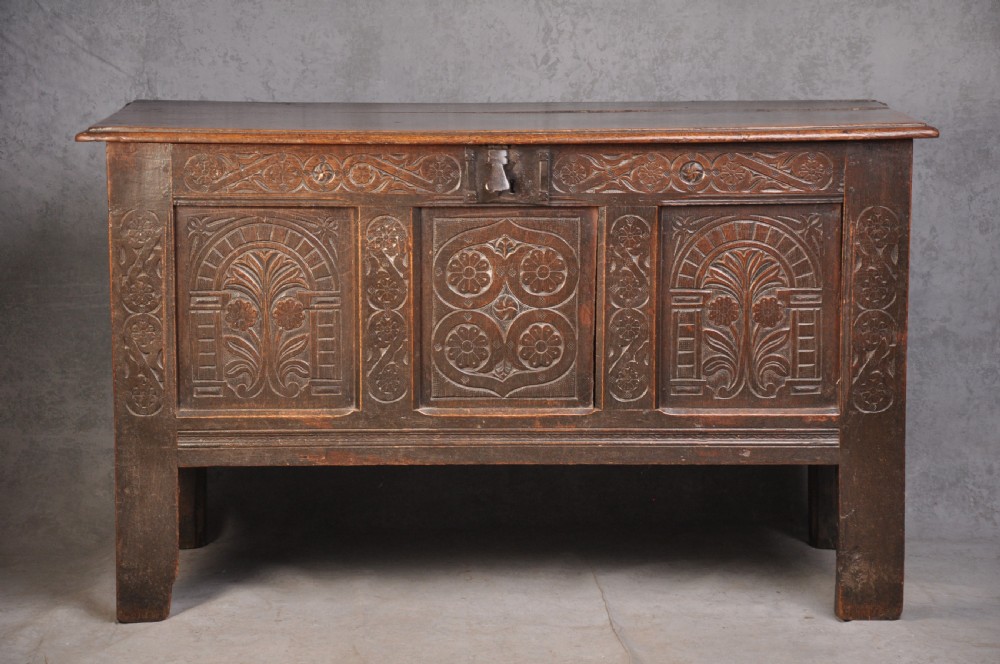 A dark brown 17th century carved oak coffer featuring three carved front panels with foliate motifs and an iron lock plate.