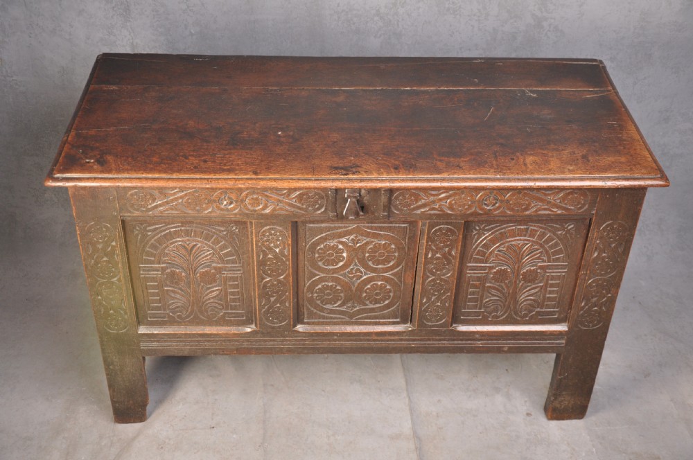 A dark brown 17th century carved oak coffer featuring three carved front panels with foliate motifs and an iron lock plate. View III