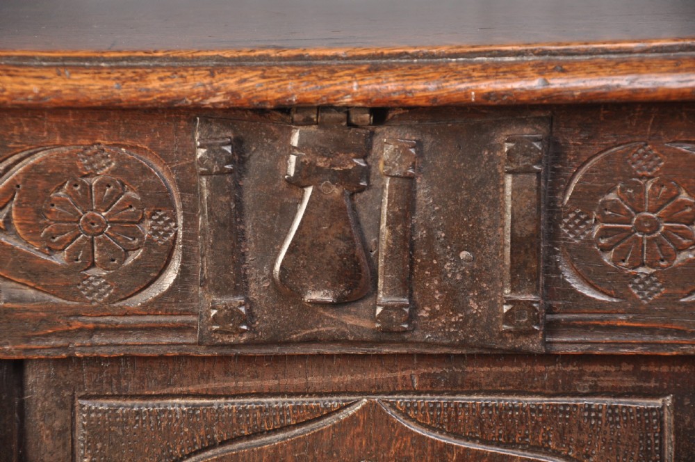 A dark brown 17th century carved oak coffer featuring three carved front panels with foliate motifs and an iron lock plate. View IV