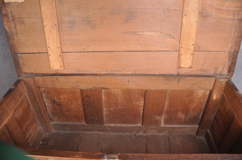 A dark brown 17th century carved oak coffer featuring three carved front panels with foliate motifs and an iron lock plate. View VII
