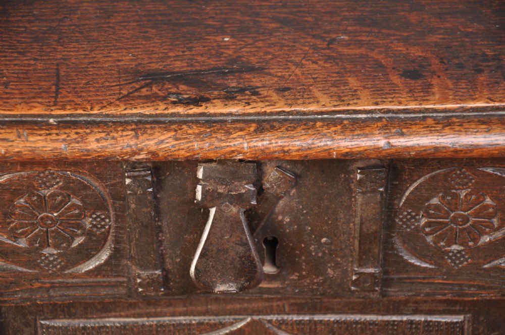 A dark brown 17th century carved oak coffer featuring three carved front panels with foliate motifs and an iron lock plate. View XII