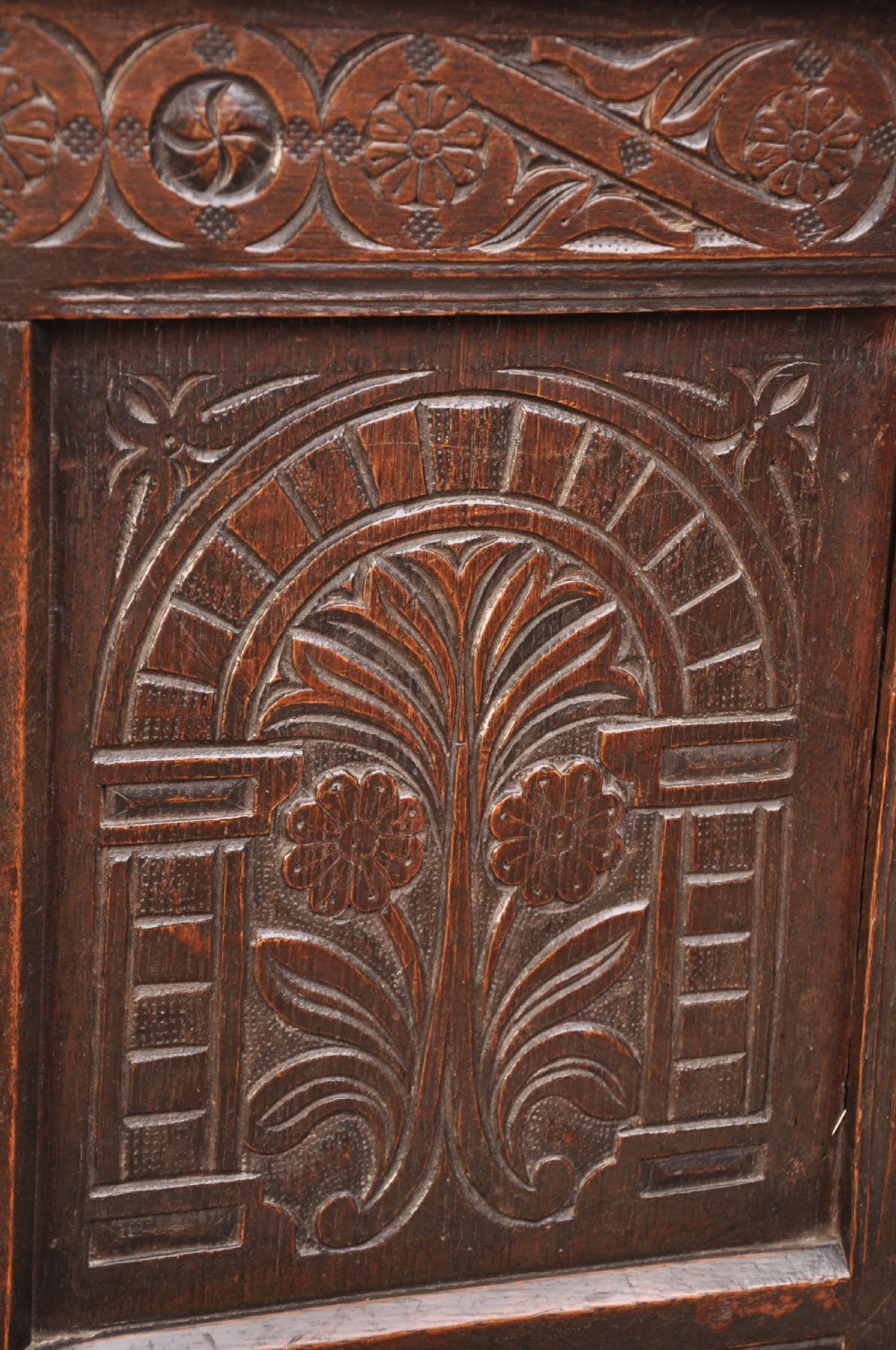A dark brown 17th century carved oak coffer featuring three carved front panels with foliate motifs and an iron lock plate. View XIV