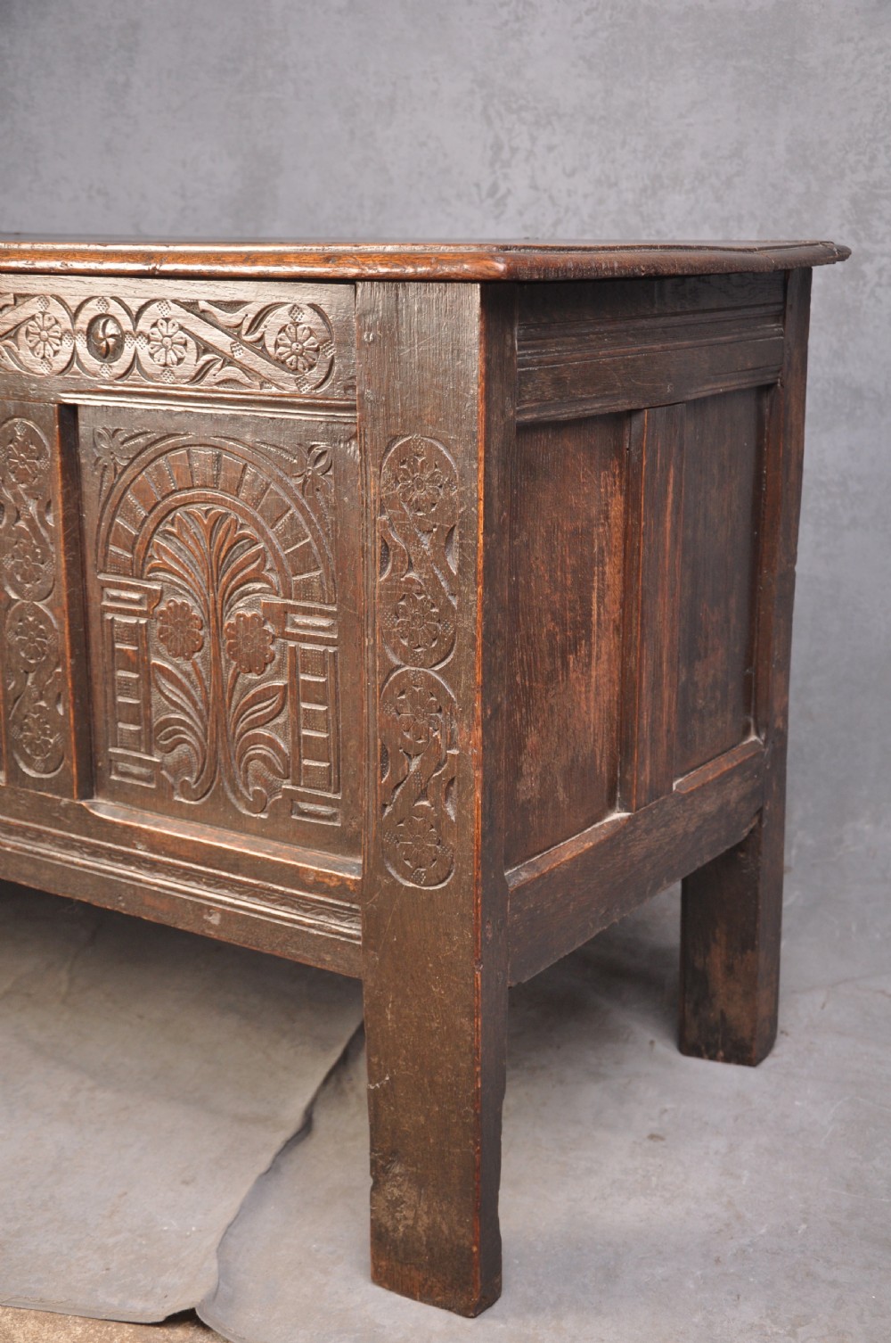 A dark brown 17th century carved oak coffer featuring three carved front panels with foliate motifs and an iron lock plate. View XVIII