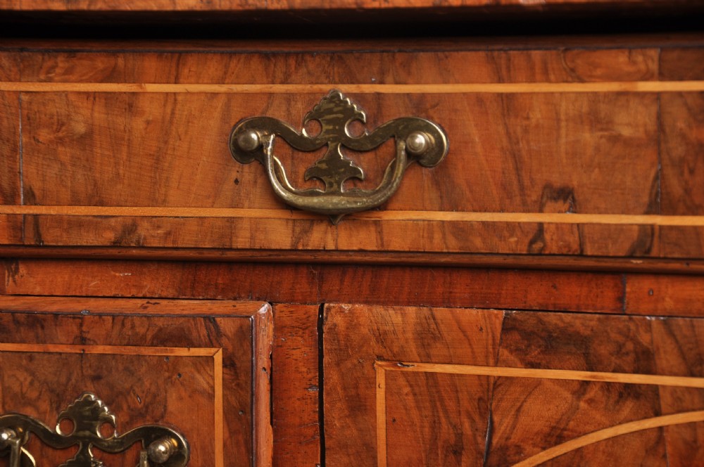 An early 18th-century walnut kneehole desk featuring crossbanded drawer fronts, brass handles, a central recessed cupboard, and bracket feet. View IV