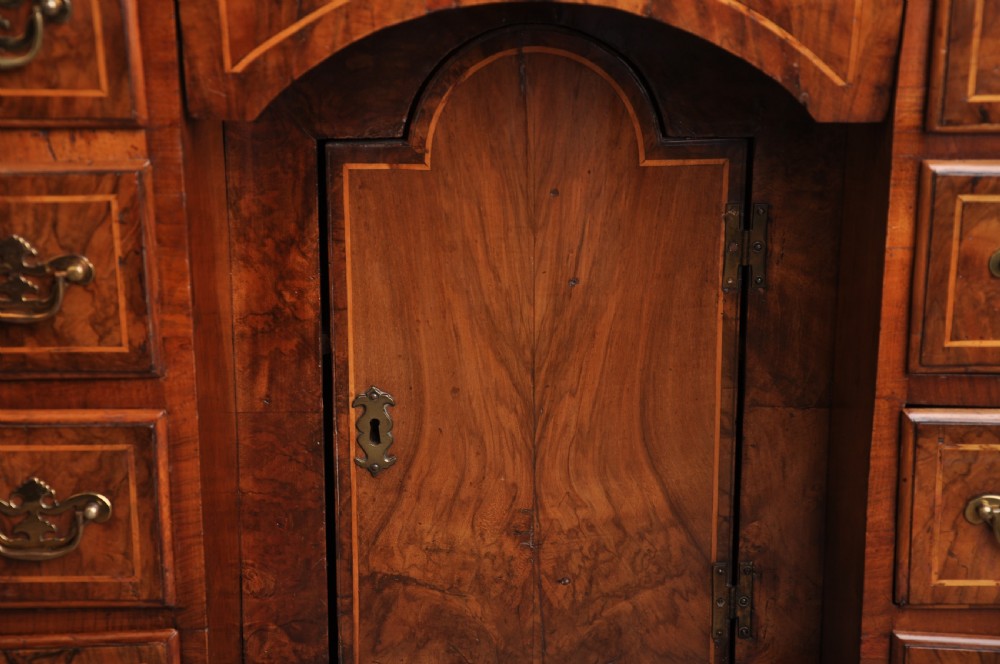 An early 18th-century walnut kneehole desk featuring crossbanded drawer fronts, brass handles, a central recessed cupboard, and bracket feet. View VII