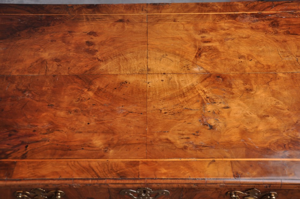 An early 18th-century walnut kneehole desk featuring crossbanded drawer fronts, brass handles, a central recessed cupboard, and bracket feet. View VIII