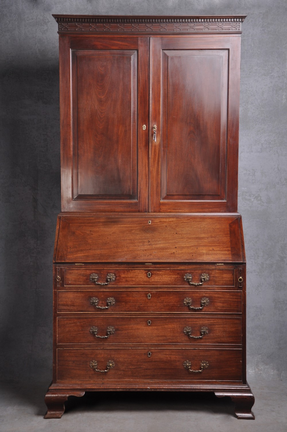 An 18th-century mahogany bureau bookcase featuring a blind two-door upper cabinet, a slant-front writing slope, four long drawers, and bracket feet.