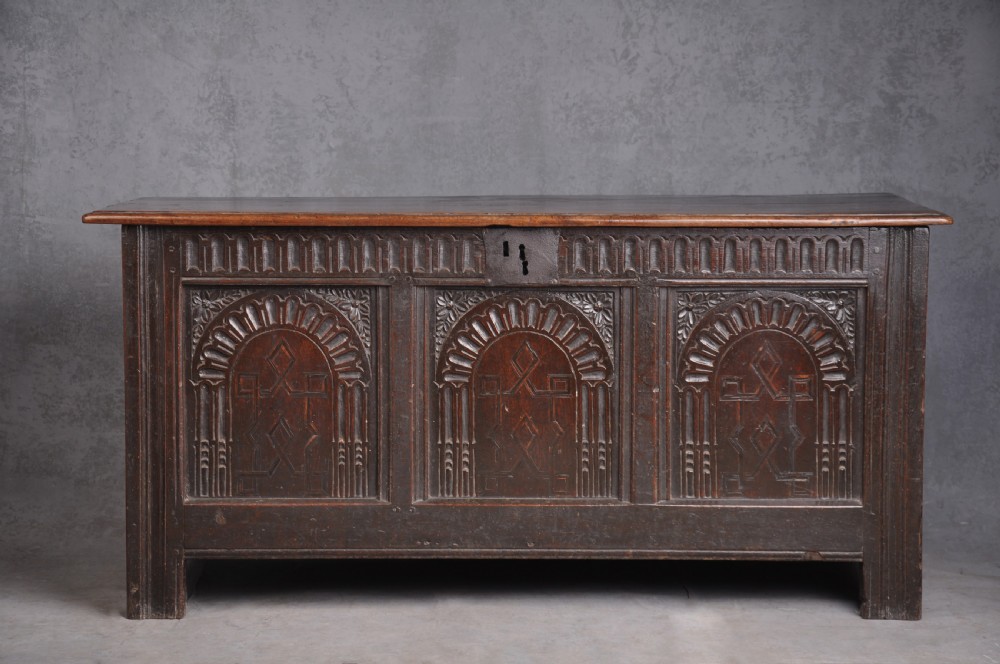 A dark oak three-panel coffer featuring relief-carved arches, geometric strapwork, a carved frieze, and a central iron keyhole plate.