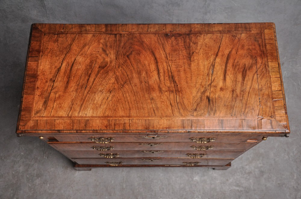 An early eighteenth century walnut bachelor chest featuring a fold-over top, four graduated drawers with brass handles, and bracket feet. View II