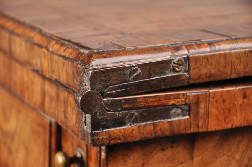 An early eighteenth century walnut bachelor chest featuring a fold-over top, four graduated drawers with brass handles, and bracket feet. View V