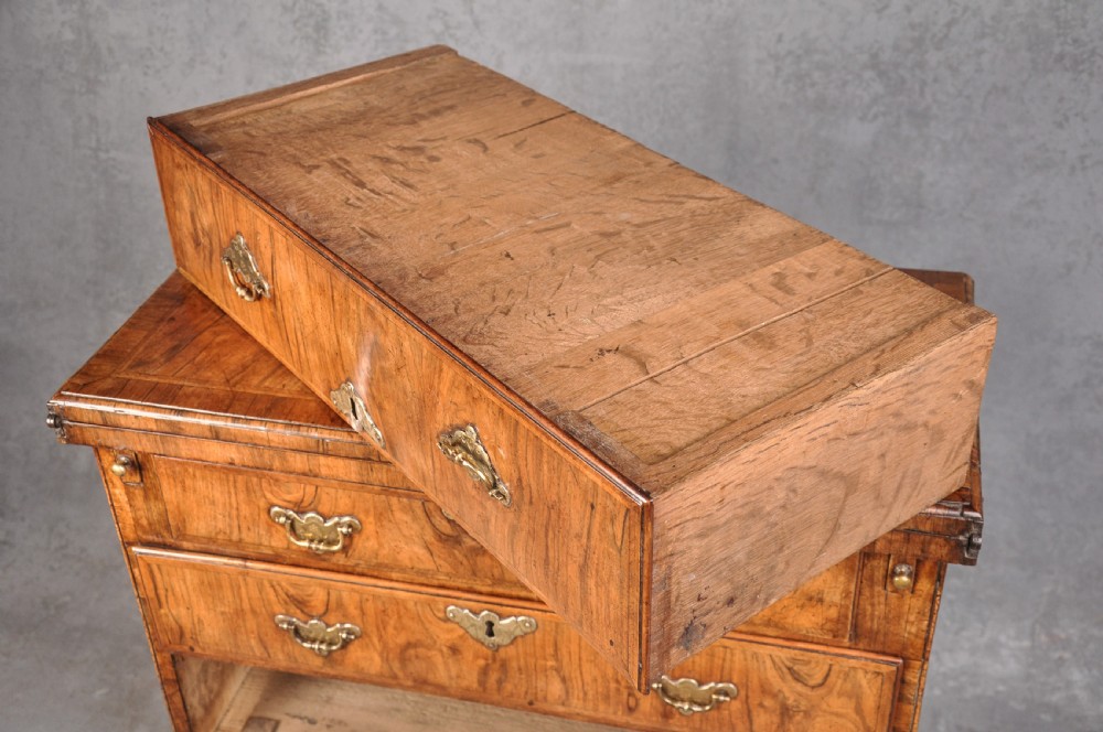 An early eighteenth century walnut bachelor chest featuring a fold-over top, four graduated drawers with brass handles, and bracket feet. View VI