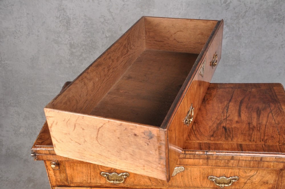 An early eighteenth century walnut bachelor chest featuring a fold-over top, four graduated drawers with brass handles, and bracket feet. View VII