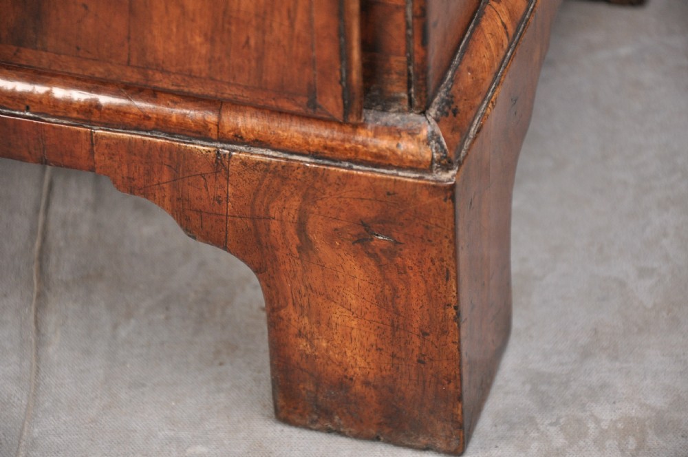 An early eighteenth century walnut bachelor chest featuring a fold-over top, four graduated drawers with brass handles, and bracket feet. View X