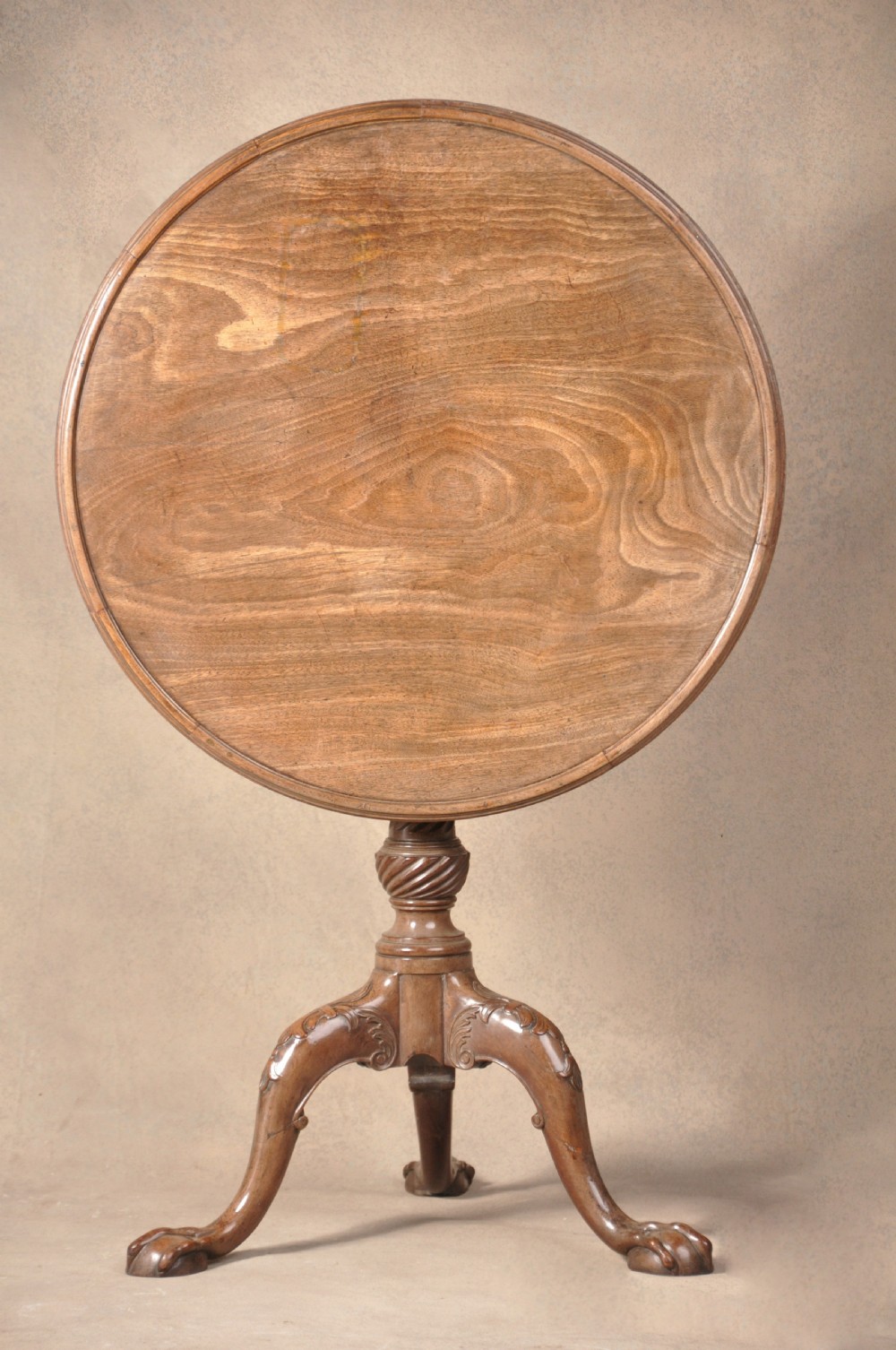 An 18th-century mahogany tilt-top tripod table shown with its circular surface locked vertically, revealing a spiral-carved pedestal and cabriole legs ending in claw and ball feet.