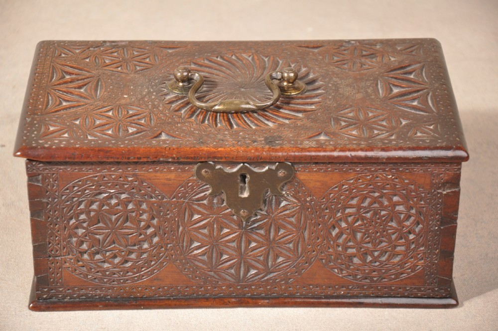A dark brown antique wooden box with detailed geometric chip-carved rosette patterns across the top and front, featuring a brass handle and keyhole escutcheon.