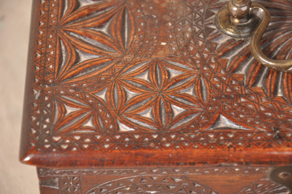A dark brown antique wooden box with detailed geometric chip-carved rosette patterns across the top and front, featuring a brass handle and keyhole escutcheon. View II