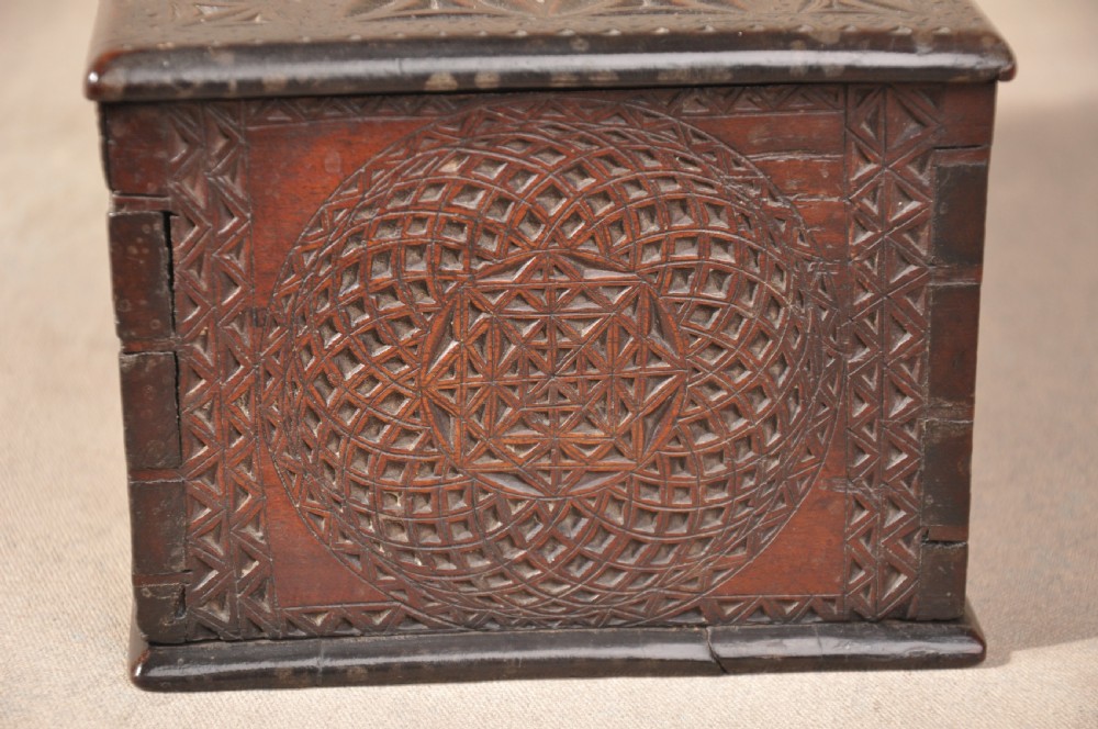 A dark brown antique wooden box with detailed geometric chip-carved rosette patterns across the top and front, featuring a brass handle and keyhole escutcheon. View III