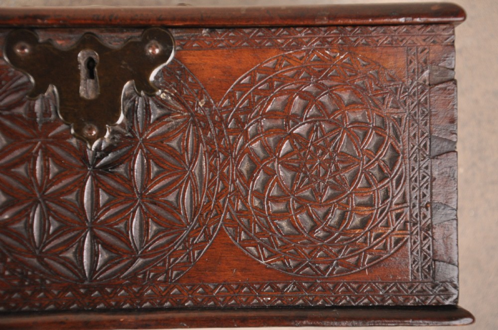 A dark brown antique wooden box with detailed geometric chip-carved rosette patterns across the top and front, featuring a brass handle and keyhole escutcheon. View IV