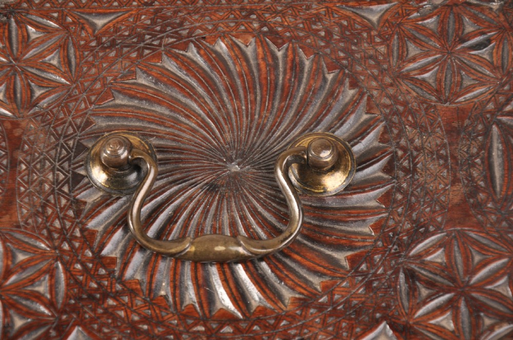 A dark brown antique wooden box with detailed geometric chip-carved rosette patterns across the top and front, featuring a brass handle and keyhole escutcheon. View V