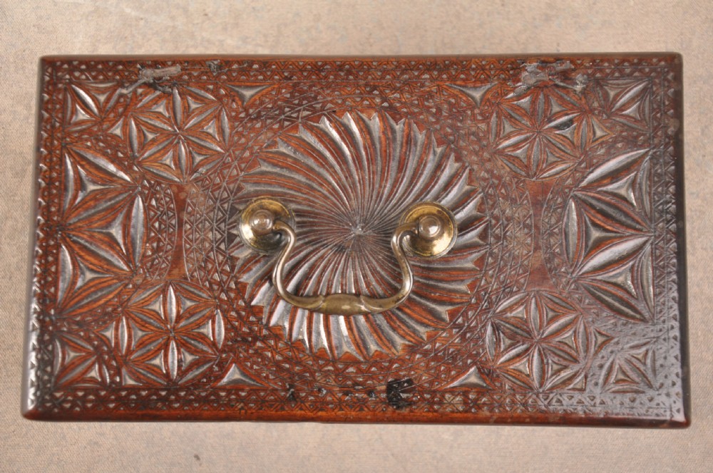 A dark brown antique wooden box with detailed geometric chip-carved rosette patterns across the top and front, featuring a brass handle and keyhole escutcheon. View VI