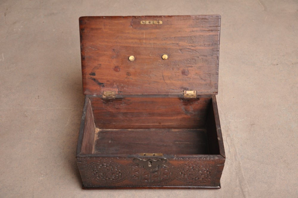 A dark brown antique wooden box with detailed geometric chip-carved rosette patterns across the top and front, featuring a brass handle and keyhole escutcheon. View VII