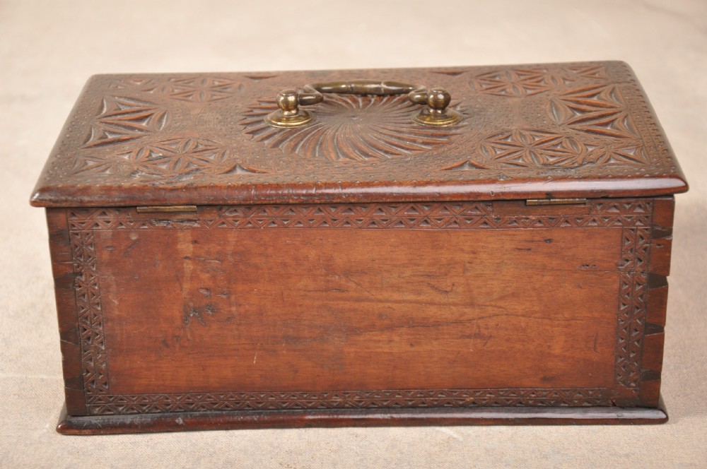 A dark brown antique wooden box with detailed geometric chip-carved rosette patterns across the top and front, featuring a brass handle and keyhole escutcheon. View VIII