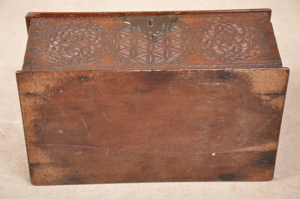 A dark brown antique wooden box with detailed geometric chip-carved rosette patterns across the top and front, featuring a brass handle and keyhole escutcheon. View IX