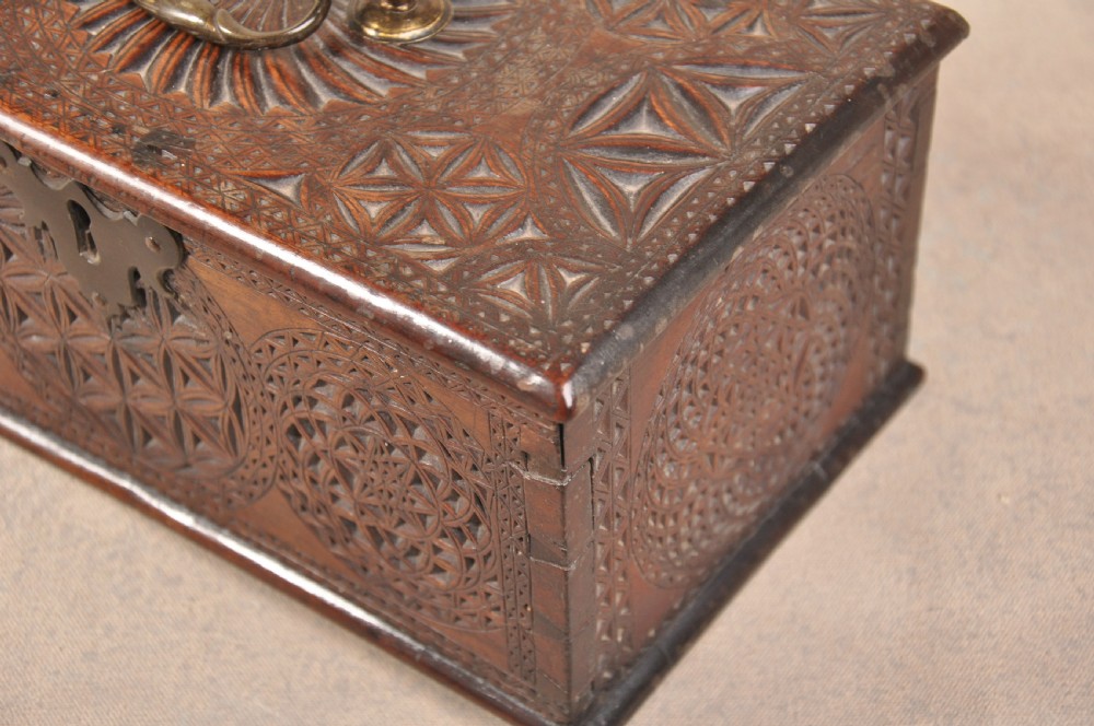 A dark brown antique wooden box with detailed geometric chip-carved rosette patterns across the top and front, featuring a brass handle and keyhole escutcheon. View X
