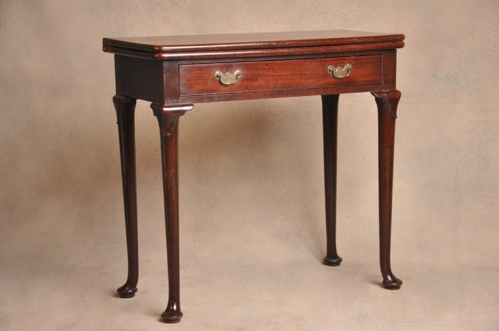 A mid-18th-century mahogany fold-over tea table featuring a single frieze drawer with brass handles and slender cabriole legs ending in pad feet.