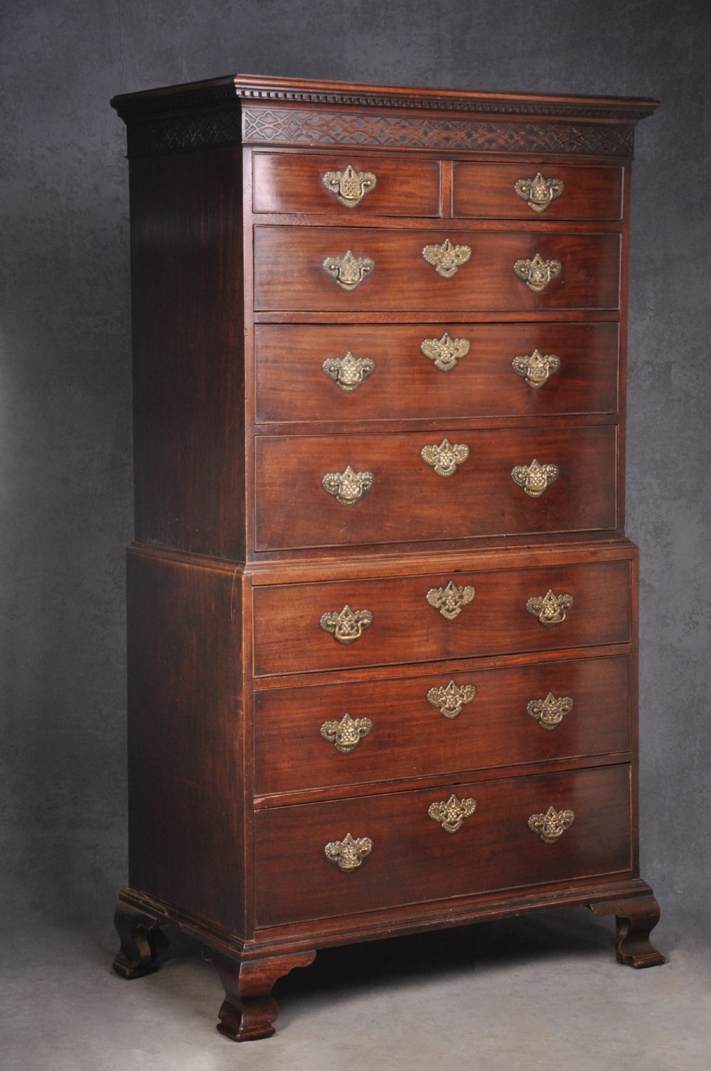 An 18th-century mahogany tallboy featuring two sections of graduated drawers, brass handles, carved blind fretwork frieze, and ogee bracket feet.