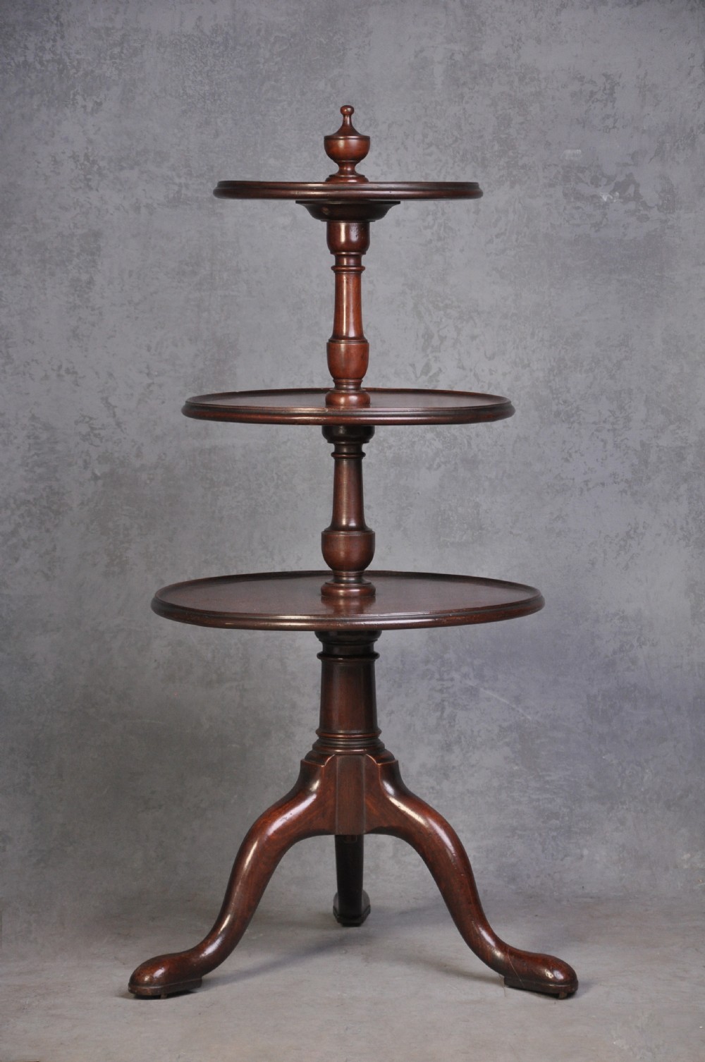 An 18th-century dark mahogany dumb waiter featuring three graduated circular dish trays supported by a turned central column on tripod cabriole legs.