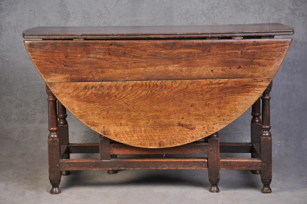 A seventeenth-century oak gateleg table shown with drop leaves folded down, featuring turned legs and low box stretchers.