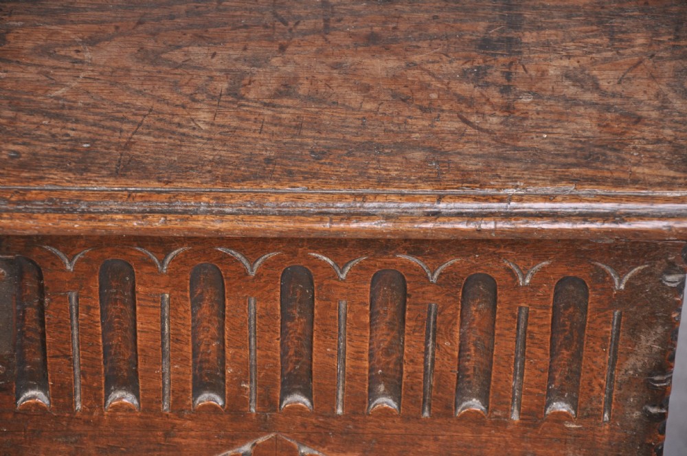 A dark carved oak plank coffer featuring twin carved diamond lozenges, a carved arched top frieze, and a central iron lockplate. View III