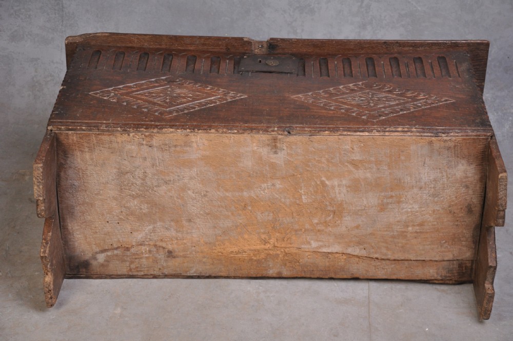 A dark carved oak plank coffer featuring twin carved diamond lozenges, a carved arched top frieze, and a central iron lockplate. View VI