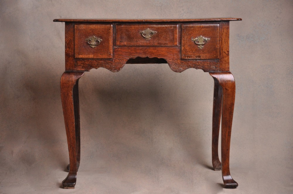 An 18th-century George I oak lowboy featuring three drawers with brass backplate handles, a shaped apron, and four cabriole legs. View II