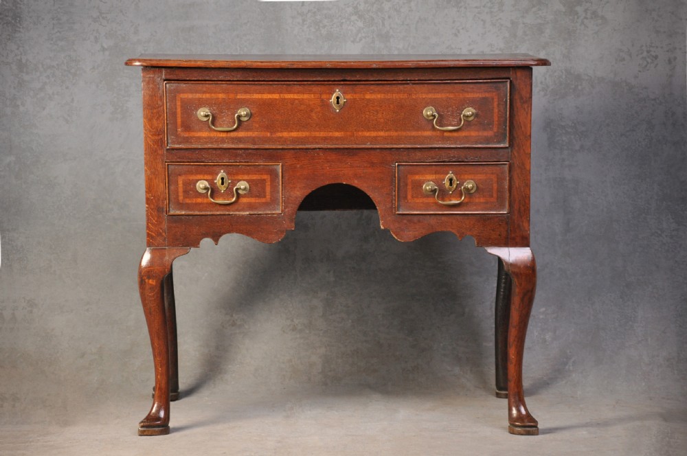 An 18th-century oak lowboy table featuring three inlaid drawers, brass swan-neck handles, an arched apron, and cabriole legs.