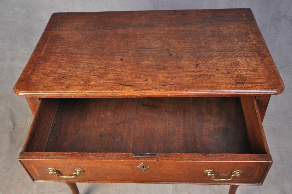 An 18th-century oak lowboy table featuring three inlaid drawers, brass swan-neck handles, an arched apron, and cabriole legs. View VI