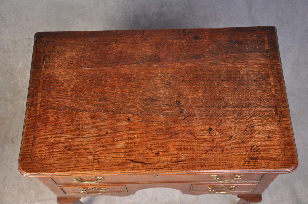 An 18th-century oak lowboy table featuring three inlaid drawers, brass swan-neck handles, an arched apron, and cabriole legs. View VII