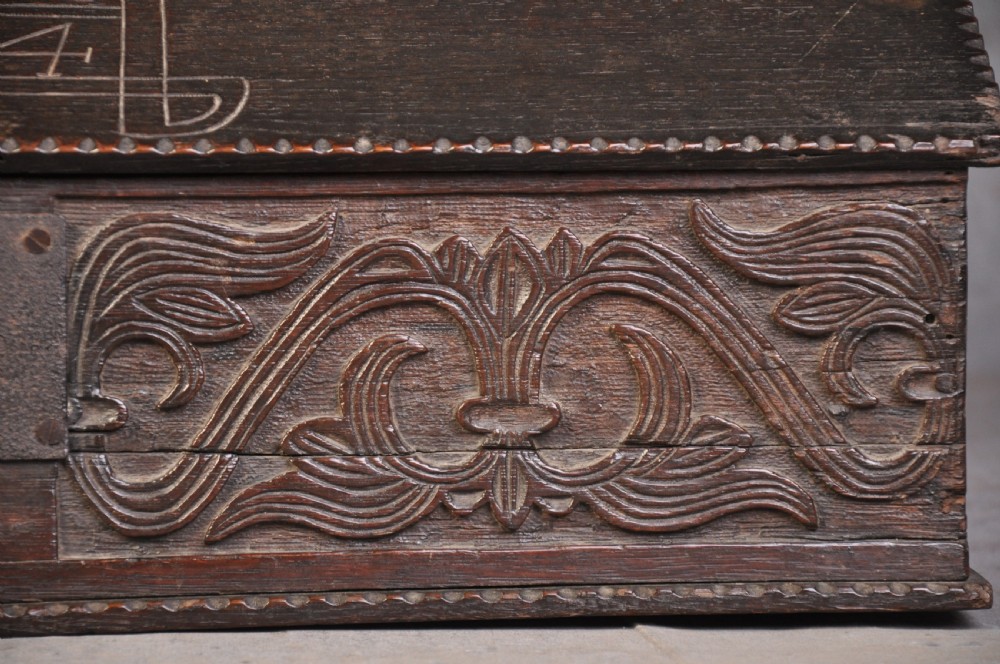 A dark carved oak desk box featuring a sloped lid incised with the date 1664 and initials, resting above foliate carved front panels with iron fittings. View III