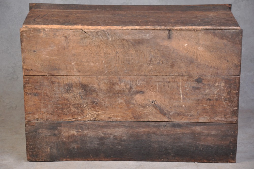 A dark carved oak desk box featuring a sloped lid incised with the date 1664 and initials, resting above foliate carved front panels with iron fittings. View V