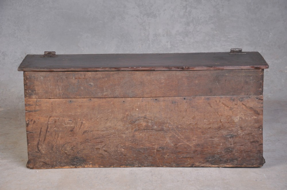 A dark carved oak desk box featuring a sloped lid incised with the date 1664 and initials, resting above foliate carved front panels with iron fittings. View VI