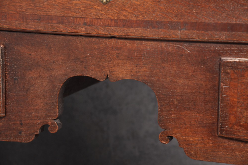 An early 18th-century oak chest on stand featuring two-part construction, multiple drawers with brass drop handles, a shaped apron, and slender cabriole legs. View V