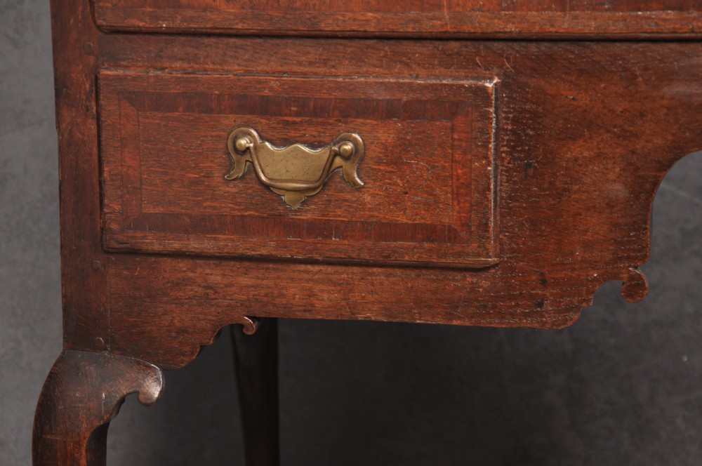 An early 18th-century oak chest on stand featuring two-part construction, multiple drawers with brass drop handles, a shaped apron, and slender cabriole legs. View VI