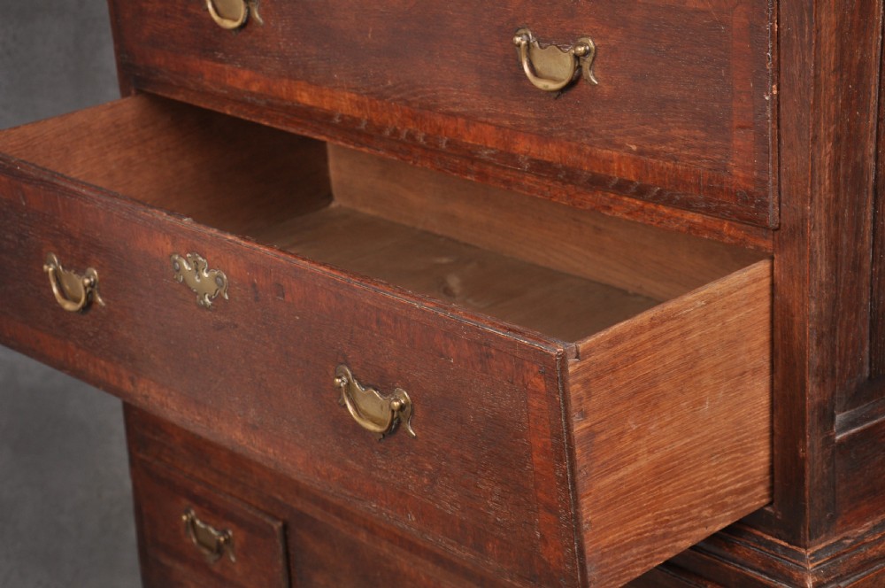 An early 18th-century oak chest on stand featuring two-part construction, multiple drawers with brass drop handles, a shaped apron, and slender cabriole legs. View VII