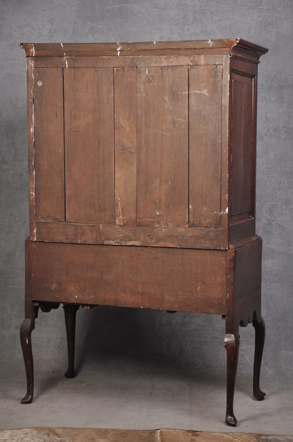 An early 18th-century oak chest on stand featuring two-part construction, multiple drawers with brass drop handles, a shaped apron, and slender cabriole legs. View XI