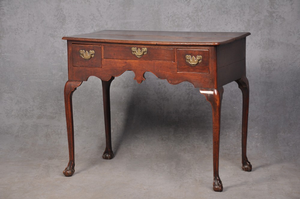 An 18th-century cherrywood lowboy featuring three drawers with brass batwing handles, a shaped apron, and cabriole legs with ball-and-claw feet.