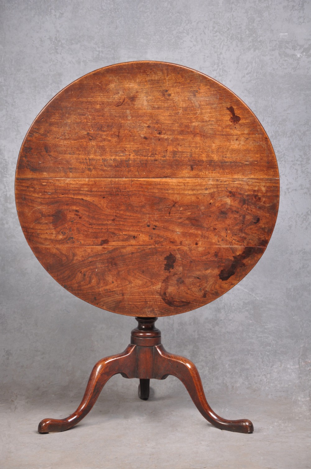 An 18th-century cherrywood tripod table featuring a circular tilt top shown upright, supported by a turned central column and three cabriole legs with pad feet.