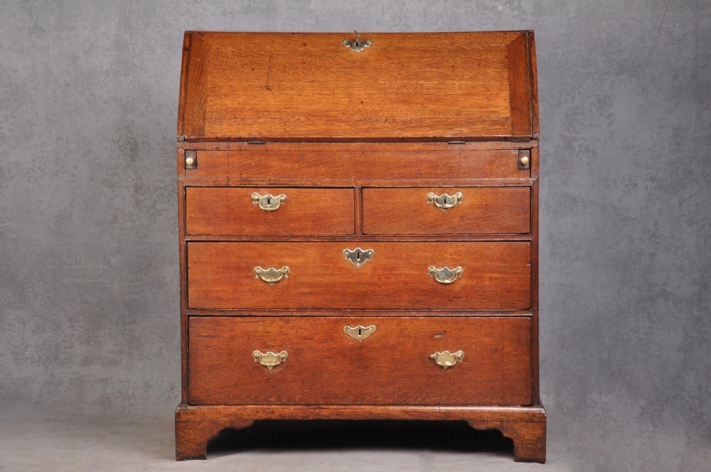 An early eighteenth-century oak bureau featuring a slanted drop-front desk above graduated drawers with brass drop handles and bracket feet. View III