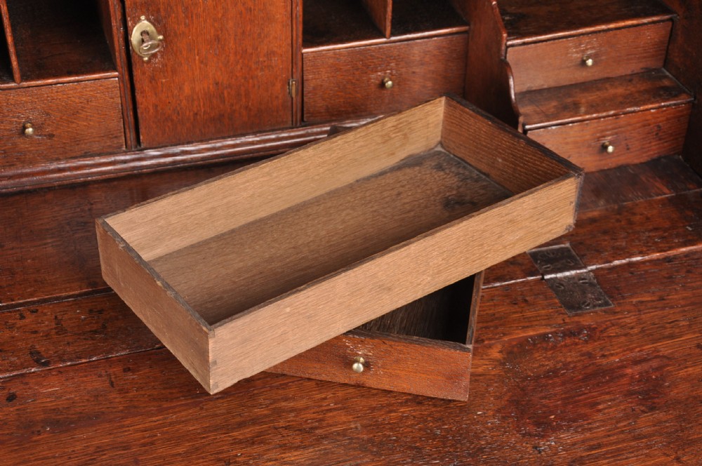 An early eighteenth-century oak bureau featuring a slanted drop-front desk above graduated drawers with brass drop handles and bracket feet. View VII