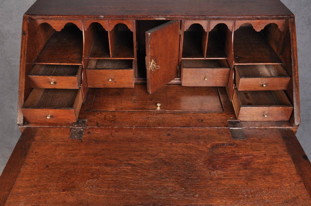 An early eighteenth-century oak bureau featuring a slanted drop-front desk above graduated drawers with brass drop handles and bracket feet. View IX